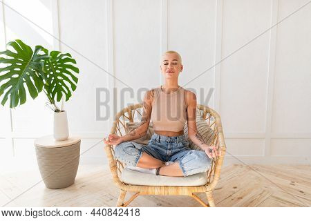 Wellness Concept. Calm Young Lady Meditating In Whicker Chair, Sitting In Lotus Position With Closed