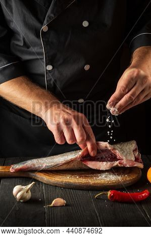 Professional Chef Prepares Fresh Fish Sprinkling Salt. Preparing To Cook Fish Food. Working Environm