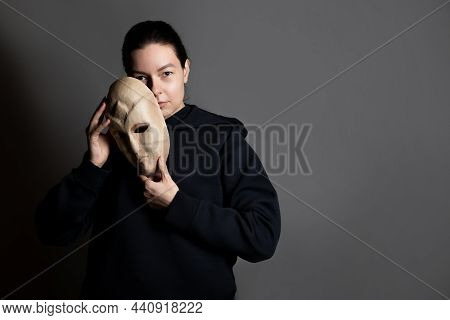 Hiding Behind A Mask, A Young Woman In A Dark Hoodie Hides Her Face With A Mask, The Concept Of Self