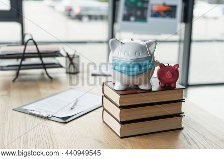 Piggy Banks With Medical Mask On Codex Books Near Blurred Contract On Desk, Anti-corruption Concept