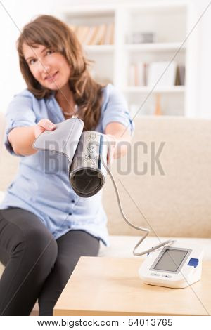 Beautiful woman checking her blood pressure at home and presenting pressure monitor cuff
