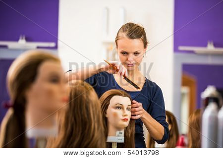 Pretty female hairdresser/haidressing apprentice/student training on an apprentice head