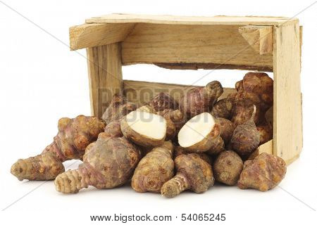 bunch of topinambur roots (helianthus tuberosus) and a cut one in a wooden crate on a white background