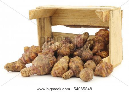 bunch of topinambur roots (helianthus tuberosus) in a wooden crate on a white background