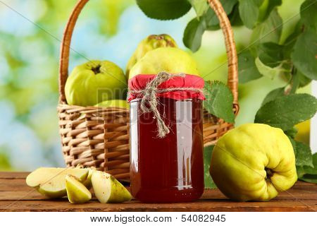 jar of jam and quinces with leaves in basket, on green background