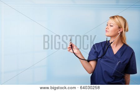 Pretty young nurse in hospital listening to empty copy space with sthetoscope