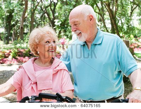 Active senio couple ride their bicycles through a park.  