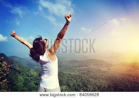 young woman cheering open arms at mountain peak