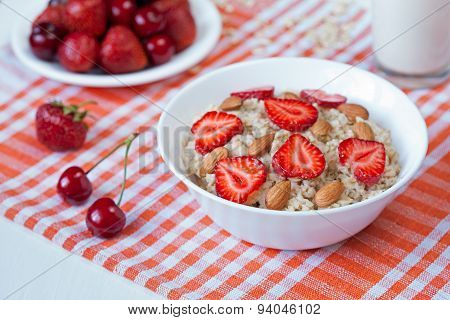Helathy breakfast oatmeal porridge with strawberry, cherries and almond nuts in white dish on kitche