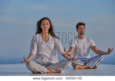 young couple practicing yoga at sunset in modern home terace with ocean and sunset in background
