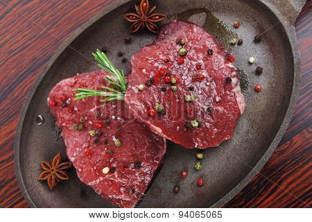 fresh raw beef fillet mignon on old retro style cast iron pan over retro wood table as background