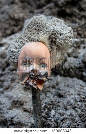 Beheaded girl doll with scary melted face on a grey ash background