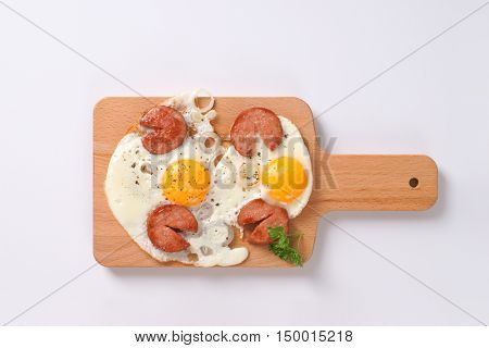 fried eggs with sliced sausage on wooden cutting board