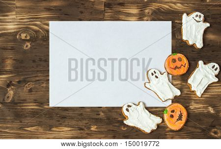 Funny delicious ginger homemade biscuits for Halloween on the dark wooden table with sheet of papper as a space for text. horizontal view from above. Halloween cookies