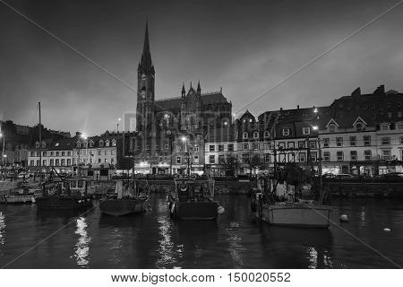 Port, houses, restaurants, shops, bars, pubs and Cathedral at night in Cobh, Ireland. Famous tourist seaport town and popular touristic destination. Black and white