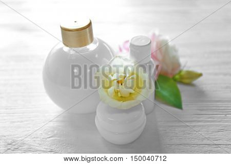 Cosmetic bottles and eustoma flowers on light wooden background