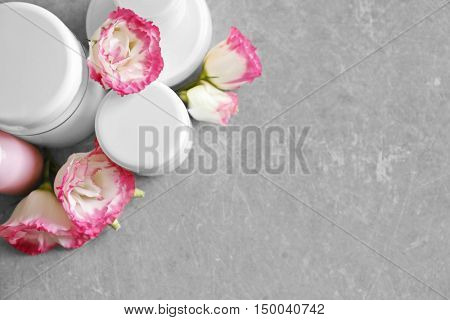 Cosmetic bottles and eustoma flowers on light wooden background