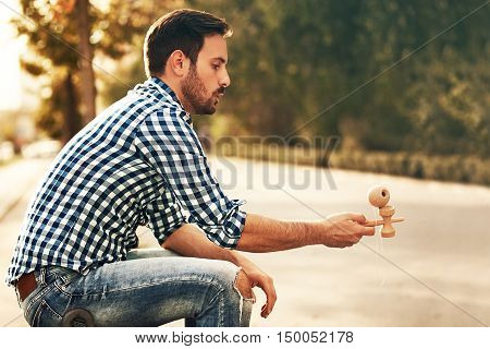 Young man is enjoying outside and playing by kendama.