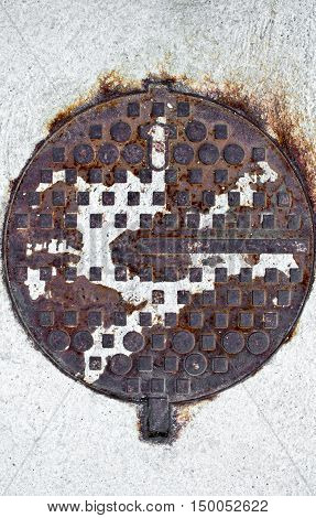 Old rusty corroded manhole cover on a white road concrete