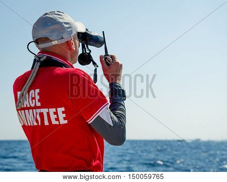 Sailing race referee is watching at his binocular, and talking by marine VHF radio. Sardinia, Italy.