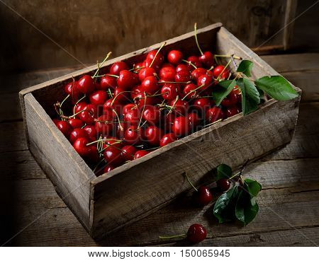 uicy red cherries in a wooden box on a dark background