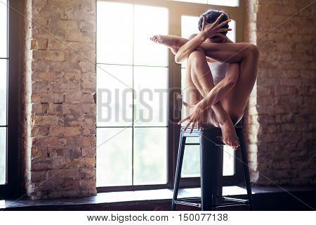 Achieving the mastery. Talented hard working attractive dancer sitting in a special position and hiding her face while having a dance class