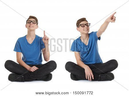 Cute teenager boy poinitng up in blue T-shirt, glasses and lotus posture over white isolated background