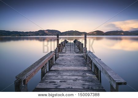 Wooden pier or jetty on blue lake sunset and sky reflection water. Long exposure Versilia Massaciuccoli Tuscany Italy.