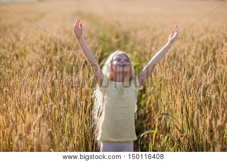little blonde girl in wheat field rising up her hands and closed eyes
