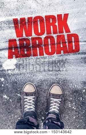 Work abroad title on the pavement above which is young male student standing and making decision to travel to foreign country and find a job
