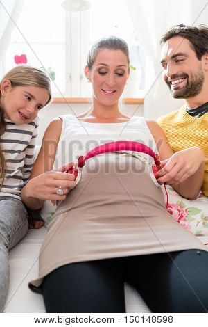 Father, daughter and pregnant mum using headphone for early musical intervention on mothers belly
