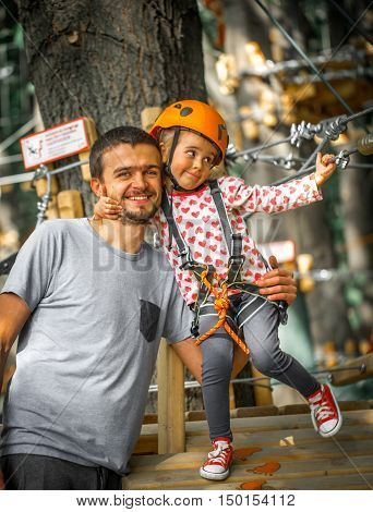 sports happy child with father climbs over the ropes beautiful girl in the outfit climbing fun in the forest on ropes and different obstacles family friendly