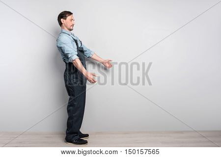 Much work to do. leasant diligent senior man holdign truck and workign while standing isolated on grey background
