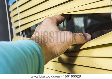 Closeup of hand opening venetian blinds. yellow shutters