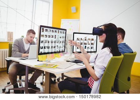 Yoiung female executive enjoying augmented reality headset with colleagues sitting at creative office