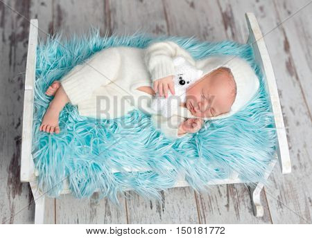 resting newborn baby in white jumper with toy on a little bed with blue furry blanket