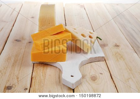 various types of fresh raw aged delicatessen cheese on white plate over light wooden table cheddar edam swiss