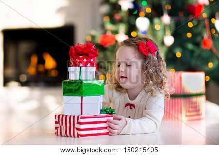 Family on Christmas morning at fireplace. Kids opening Xmas presents. Children under Christmas tree with gift boxes. Decorated living room with traditional fire place. Cozy warm winter day at home.