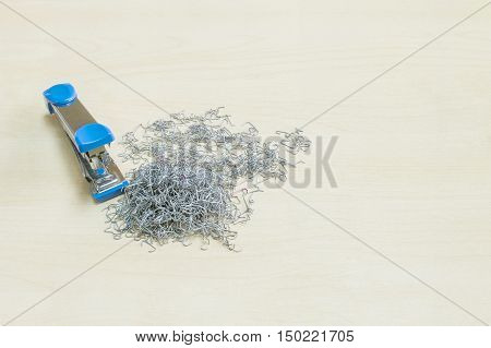 Closeup pile of used staples with blue stapler office equipment on blurred wood desk in office room textured background under window light