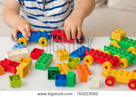 Close up of child's hands playing with colorful plastic bricks at the table. Toddler having fun and building out of bright constructor bricks. Early learning. stripe background. Developing toys
