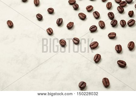 Coffee beans are lying on white stone textured surface, forming a background.