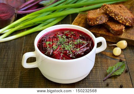 Red borscht soup with dill in white bowl on wooden table