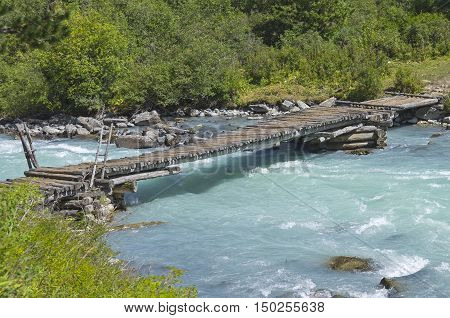 Old wooden bridge at the end of the Kucherla lake whence the river Kucherla follows. Altai Mountains Russia. Sunny summer day.