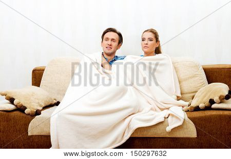 Smiling loving couple sitting on couch with blanket