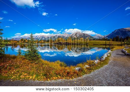 Path around the lake. The concept of hiking. Canmore, near Banff National Park. Majestic mountains and scenic cumulus clouds are reflected in the water