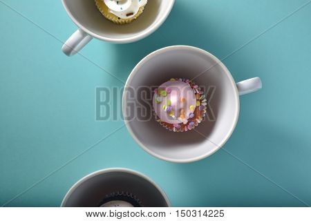 Cute looking fine quality mini cup cakes placed in white porcelene tea cups in a row. A conceptual food photography. Shot from above.