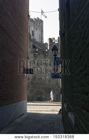 Ghent, 27 august 2016: castle of gravensteen in Ghent with tourist passing by seen from narrow old alley