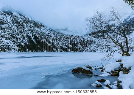 Winter day in Polish Tatra mountains, frozen Morskie Oko lake and summits in the clouds.