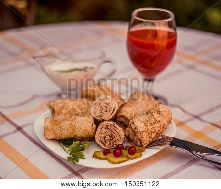 Tasty pancakes with meat on white plate closeup. Crepes stuffed with finely cut meat. glass of tomato juice and white sauce.