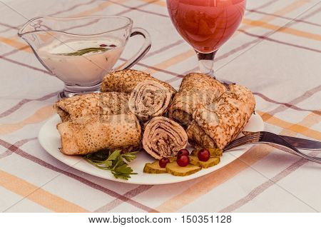 Tasty pancakes with meat on white plate closeup. Crepes stuffed with finely cut meat. glass of tomato juice and white sauce.